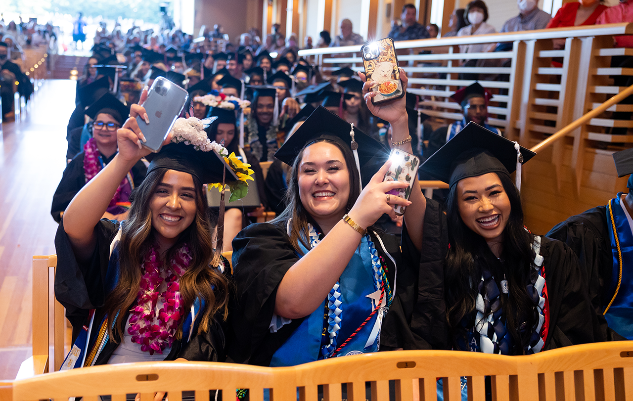Three graduates wave with cell phones