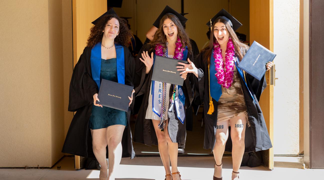 3 students walking off stage at commencement