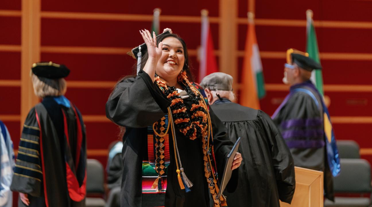 Student waiving after receiving diploma on stage