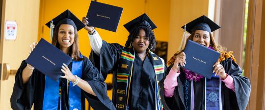 Three graduates wave diplomas