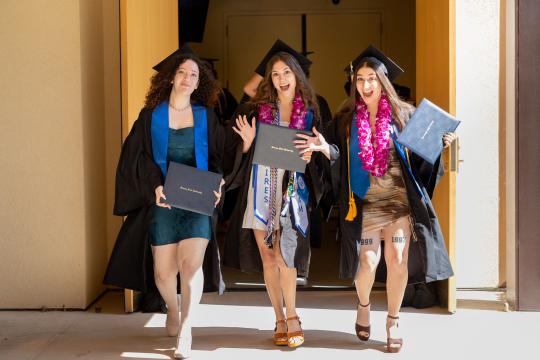 3 students walking off stage at commencement
