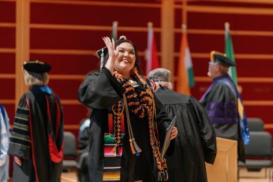 Student waiving after receiving diploma on stage